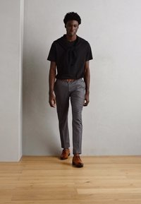 Camisa negra de manga corta con detalle anudado, pantalones gris ajustados y zapatos de cuero marrón. Textura suave y corte moderno.