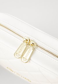 Weiße, gesteppte Tasche aus Kunstleder mit goldfarbenem Reißverschluss und zwei Zuglaschen, die mit "Valentino" geprägt sind. Glatte Textur und elegantes Design.