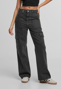 Pantalons cargo en denim noir taille haute avec des jambes larges, plusieurs poches et une finition soignée, associés à un haut noir et des baskets blanches.