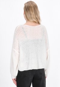 Cremfarbener Strickpullover mit lockerer Passform, weiter Ausschnitt, langen Ärmeln und geripptem Saum. Halbdurchsichtige Textur mit offenen Strickmustern.