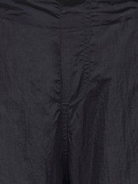 Pantalon léger noir avec une texture froissée, doté d'une ceinture lisse, de coutures visibles et d'un design minimaliste.