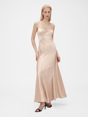 Satin, peach-colored maxi dress with thin straps, a fitted bodice, and a flowing skirt. Worn with black open-toe heels.