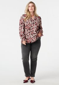 Blouse à manches longues avec imprimé animal multicolore en rouge et noir, associée à un jean slim gris foncé et des talons en vernis bordeaux.