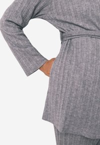 Robe en tissu texturé gris avec un motif de rayures verticales, dotée d'une taille ceinturée et de manches longues. L'ourlet est légèrement courbé.