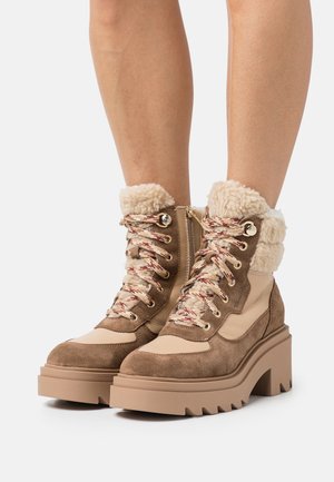 Bottes de randonnée en suède marron et cuir beige avec un col en polaire, une semelle épaisse et colorée et des lacets multicolores. Accents en matériel doré.
