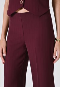 Pantaloni su misura borgogna con una fantasia a righe sottili, caratterizzati da un taglio dritto, una texture liscia e una tasca laterale discreta.
