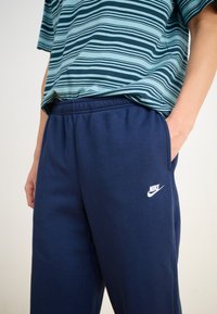Μπλε βαμβακερές φόρμες με ελαστική μέση, πλαϊνές τσέπες και λευκό λογότυπο Nike. Συνδυασμένες με μπλουζάκι ριγέ σε τιρκουάζ και ναυτικό μπλε.