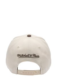 Gorra de béisbol color beige claro con un logotipo bordado en marrón de "Mitchell & Ness" en la parte posterior, que cuenta con una correa ajustable de plástico y agujeros de ventilación.