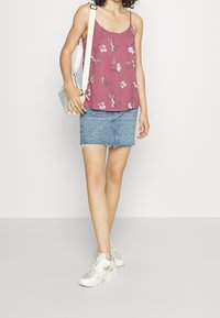 Fioletowy top na ramiączkach z kwiatowym wzorem, w zestawieniu z jasną dżinsową mini spódniczką z postrzępionym dołem. Białe sportowe sneakersy dopełniają look.