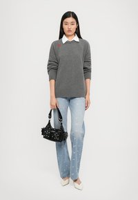 Gray sweater with a round neckline and red embroidered detail, paired with light blue flower-patterned jeans and a black handbag. White heels.