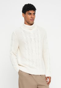Jersey de cuello alto color crema con patrón de trenzado, puños y dobladillo acanalados. Fabricado con una tela texturizada, que ofrece una apariencia acogedora.