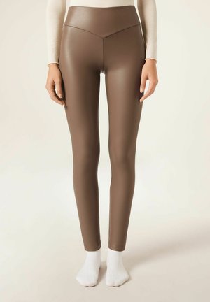 Brown faux leather leggings with a high waist and a smooth texture, fitted design, and ankle-length cut, worn with white ankle socks.