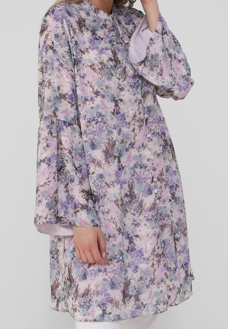 Tunique à motif floral avec des manches longues évasées. Couleurs comprenant le violet, le rose et le gris. Dotée d'un col rond et de détails de boutons.