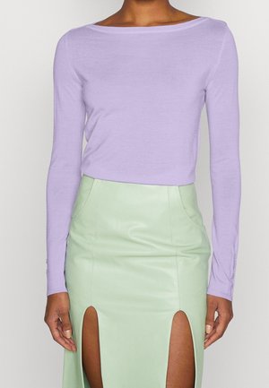 Langærmet, lavendel top lavet af blødt stof, parret med en myntgrøn læderskirt med sidesplit og tætsiddende design.