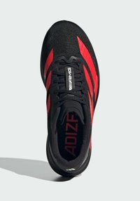 Black athletic shoe with red stripes, mesh upper, rounded toe, reinforced heel, and textured sole. Features logo on the tongue and inner lining.