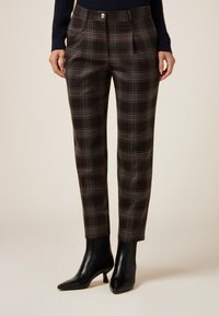 Skræddersyede brune ternede bukser med en blanding af mørke og lyse plaid-mønstre. Har en tilpasset talje og et smalt ben-design, kombineret med sorte hæle.