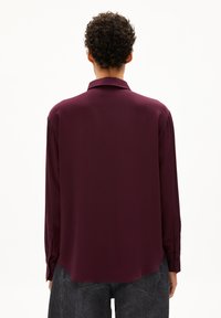 Burgundy long-sleeve shirt with a classic collar and buttoned cuffs; smooth texture; slightly curved hem for a relaxed fit.