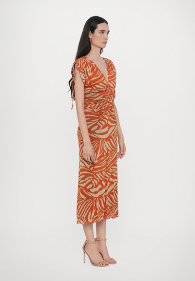 Orange och beige midjelång klänning med zebramönster, v-ringning och rynkad detaljering, med knytband och en luftig design. Sandaler syns.