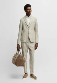 Beige geruite pak met een blazer met één knoop en tapse broeken. Witte shirt eronder. Bruine suède tas met dubbele handvatten. Beige loafers.