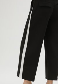 Černé kalhoty s bílým bočním pruhem, elegantní střih, rovný tvar nohavic, látka s hladkým texture, s detaily zadní kapsy.