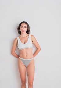 Grijze katoenen string en witte sportbeha met elastische band. Beide hebben een eenvoudig ontwerp en een gladde textuur, met minimale branding.