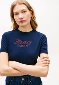 Μπλε βαμβακερό T-shirt με κόκκινο κεντημένο λογότυπο "TOMMY HILFIGER, CO." στο στήθος, με κοντά μανίκια και εφαρμοστή γραμμή.