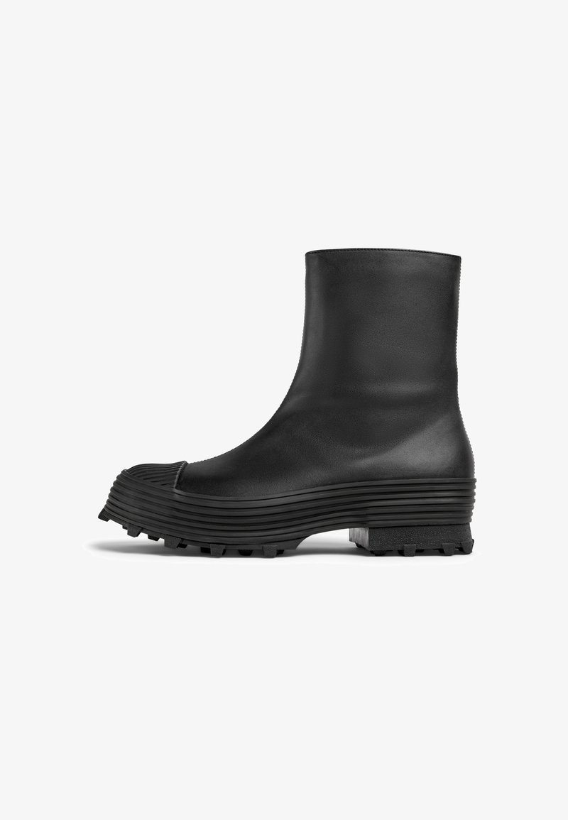 Bottine noire en cuir lisse avec une semelle structurée et nervurée et un bout arrondi, présentant une finition texturée et une semelle durable.