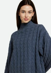 Pull torsadé à col roulé en bleu foncé, présentant un motif texturé, une coupe décontractée et des manches longues. Fabriqué en mélange de laine doux.