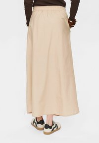 Jupe maxi beige fluide avec une taille élastique, associée à des baskets blanches et noires au fini texturé.
