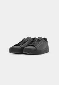 Baskets noires avec une tige en cuir lisse, bout rond, fermeture à lacets et semelle en caoutchouc texturée. Design minimaliste avec un branding subtil.