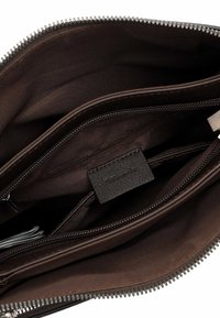 Interno di borsa in pelle marrone con numerose tasche con cerniera e tasche aperte, texture liscia e etichetta del logo sul lato.