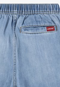 Vue arrière d'un pantalon en denim bleu clair avec une ceinture élastique et une petite poche arrière rectangulaire comportant une étiquette rouge du logo Levi's.