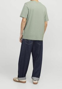 Camiseta de algodón verde con mangas cortas, combinada con jeans de mezclilla azul sueltos, puños remangados y zapatillas beige. Diseño sencillo y casual.