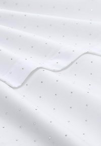 Witte stof met een gladde textuur, versierd met verspreide kleine zilveren pailletten, die een subtiel patroon over het oppervlak creëren.