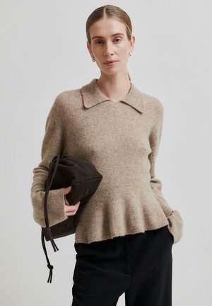 Pullover beige in lana con collo a camicia e orlo svasato, abbinato a una borsa in suede marrone scuro, con chiusura a coulisse.