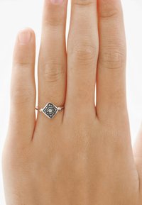 Anillo de plata en forma de diamante con un centro negro texturizado y un acento de diamante circular, flanqueado por diamantes más pequeños a cada lado.