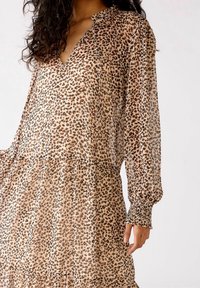 Abito leopardato traslucido in tonalità beige e marrone, con scollatura a V, arricciature ai polsini e design con orlo a strati.