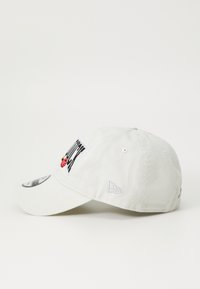 White cotton baseball cap with embroidered logo featuring a red character, curved brim, eyelets for ventilation, and logo on the side.