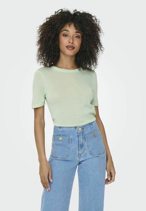 Haut vert clair à manches courtes en tissu tricoté texturé, associé à un jean taille haute bleu clair avec deux poches avant.