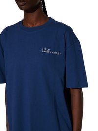 Osoba ubrana w granatowy T-shirt z białym nadrukiem "HALO 196819721981" na lewej stronie klatki piersiowej, na białym tle.