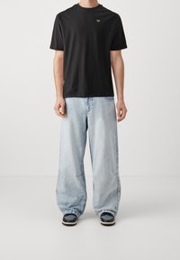 T-shirt nera in cotone con maniche corte e un piccolo logo dorato. Abbinata a jeans in denim oversize di colore blu chiaro e sneakers nere.
