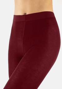 Burgunderfarbene Leggings aus weichem, dehnbarem Material. Hoher Bund mit glatter Textur und ohne sichtbare Nähte oder Verzierungen.