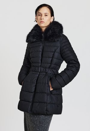 Manteau matelassé noir avec col en fourrure, ceinturé à la taille, avec une texture matelassée et une fermeture éclair à l'avant. Comprend des poches latérales.