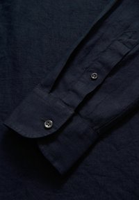 Camicia di lino blu navy con maniche, caratterizzate da un polsino con bordo arrotondato, due bottoni e una texture sottile.
