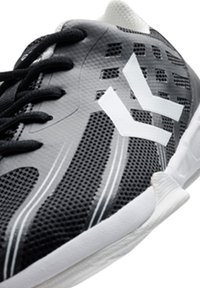 Chaussure de sport noir et blanc avec une tige en mesh à texture, des accents blancs contrastants et une semelle blanche rembourrée.