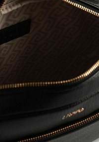 Innenraum einer schwarzen Ledertasche mit einem goldfarbenen Reißverschluss. Das Futter zeigt ein strukturiertes Muster in hellbraunen und dunkelbraunen Tönen.