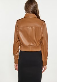 Brun imitation læder cropped jakke med ribbet talje og manchetter. Har en foldet krave og en glat, skinnende overflade.