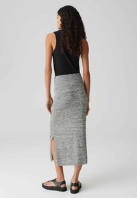 Haut sans manches noir associé à une jupe midi en tricot grise avec une texture subtile et une fente sur le côté, portée avec des sandales à brides chevilles noires.