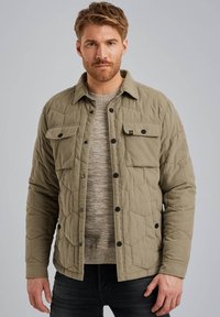 Chaqueta acolchada verde oliva con botones a presión negros, dos bolsillos en el pecho y un suéter de punto texturizado debajo.