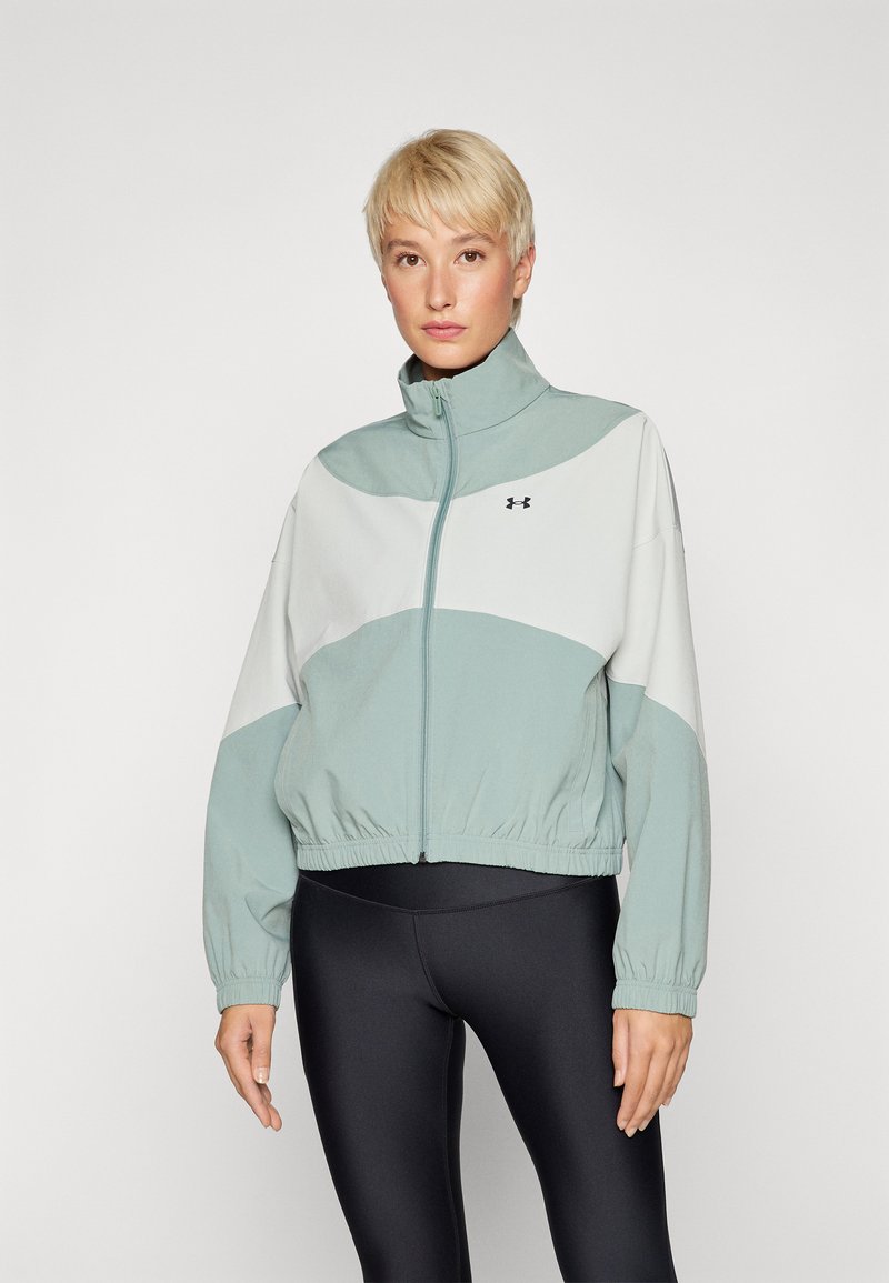 Chaqueta recortada en verde claro y blanco con un alto cuello, puños elásticos y cinturilla. Cuenta con cierre de cremallera y logo de la marca en el pecho.